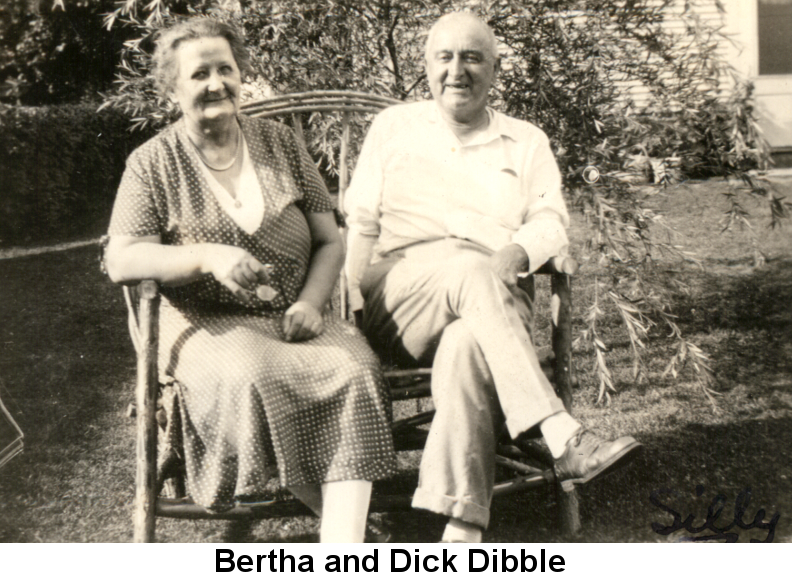 Black and white photo of Bertha and her husband Dick Dibble sitting on a wicker loveseat in front of a young willow tree, some time in the 1930s.